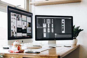 Desk with two monitors. Graphic design software open on monitors.