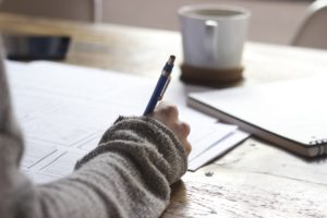 Woman writing on paper with cup of coffee in the background.